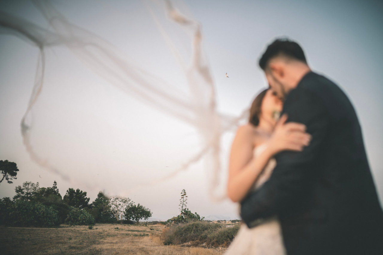 F.A.Q. Wedding Photography - Bacio Sposi con Velo al Vento e gabbiano nello Sfondo